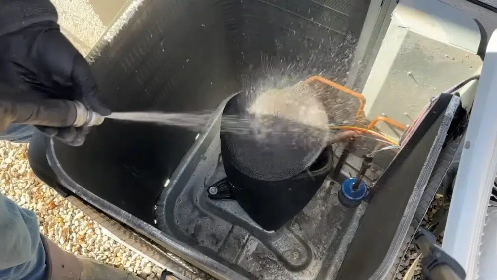 Technician spraying water to clean the AC compressor and surrounding coil during an AC maintenance service in Los Angeles County, CA.