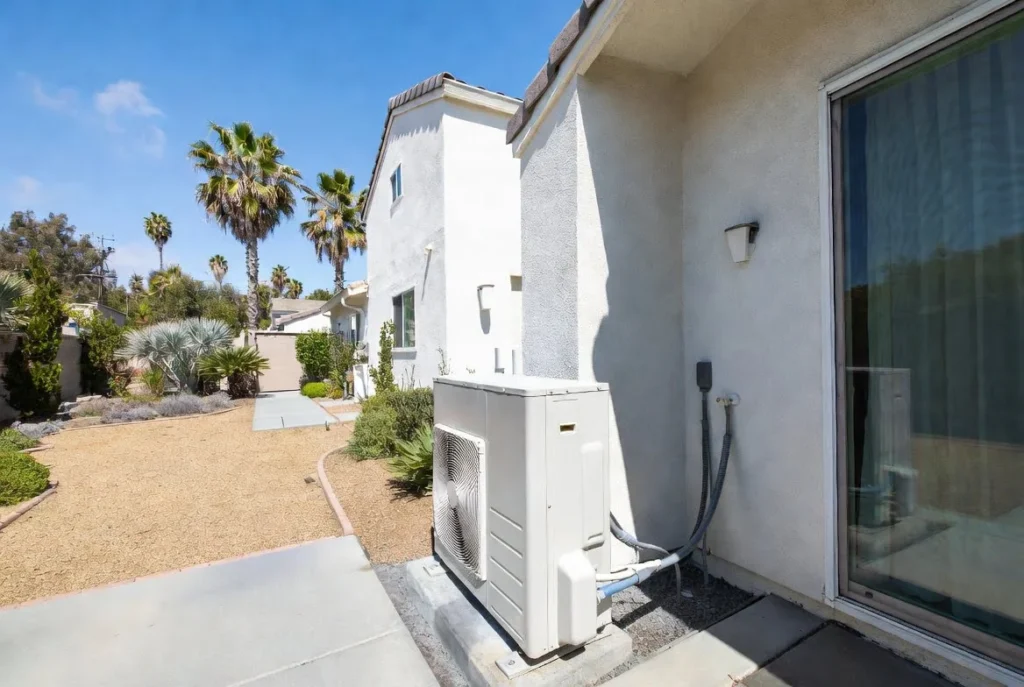 Sleek modern outdoor my heat pump unit installed next to a beautiful stucco home in sunny Los Angeles with palm trees and clear blue sky.