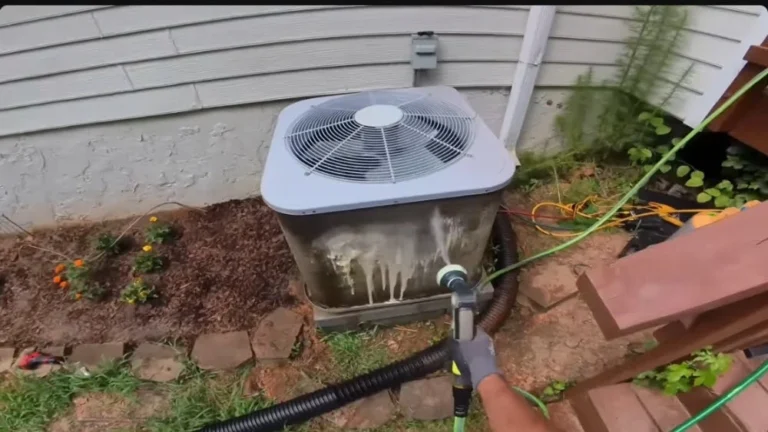 Technician rinsing an outdoor AC condenser to remove debris for local HVAC repair.