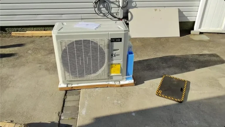 ACiQ ductless mini-split outdoor condenser positioned on a concrete driveway beside a residential home, ready for installation.