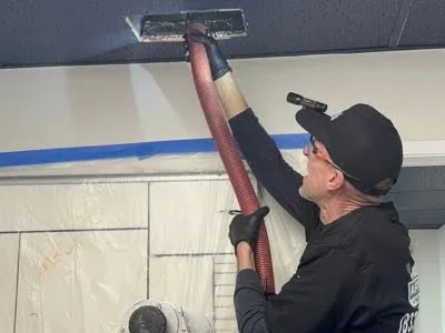 Affordable Heating and Air technician vacuuming a ceiling vent during professional air duct cleaning in Van Nuys CA.
